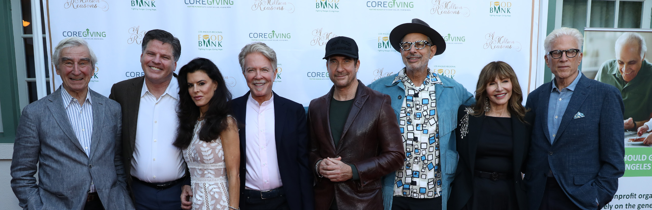 A group of eight people stands together, smiling, in front of a backdrop adorned with logos of the Los Angeles Regional Food Bank. They are dressed in a mix of formal and casual attire.