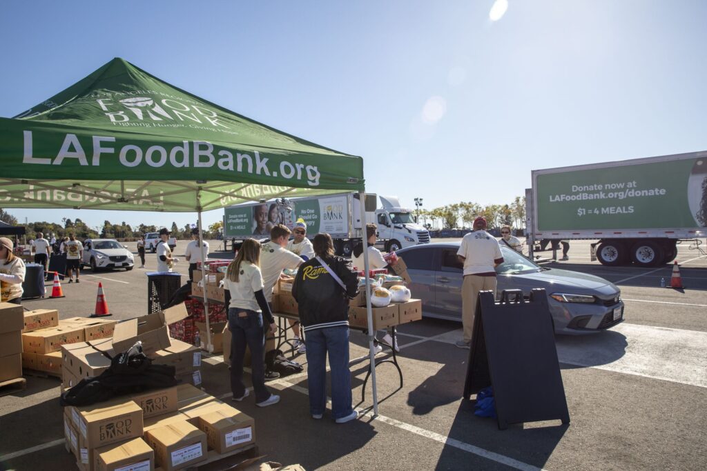 Volunteers distribute food at an outdoor drive-thru event, showcasing their dedication in an inspiring Impact Report. A green tent with 