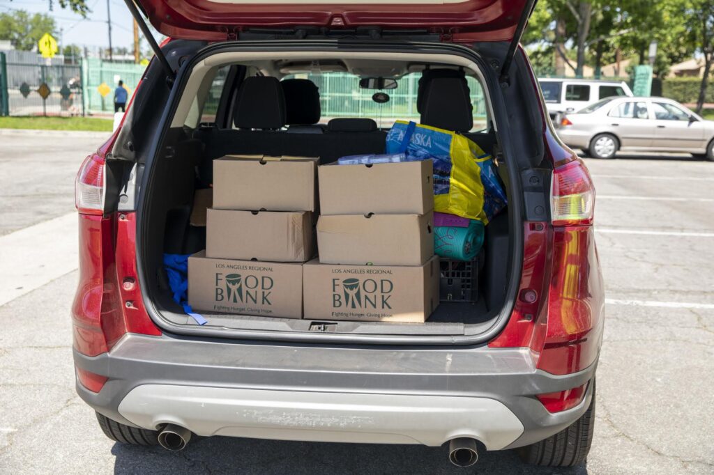 a food recipient in a red car has food boxes loaded onto trunk