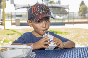 A small boy drinks his chocolate milk during a free summer meals distribution at Bristow Park during the 2023 summer