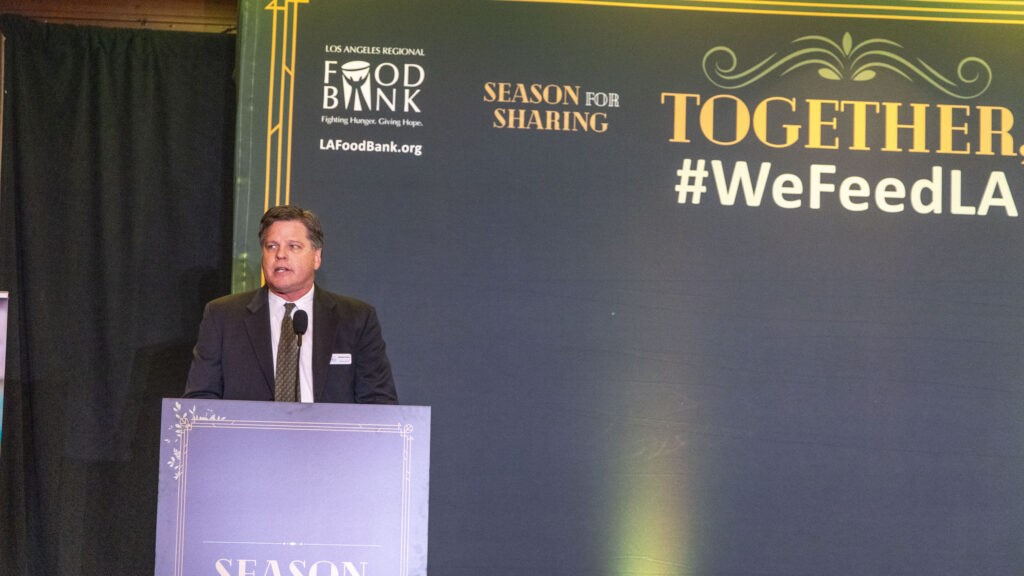 A man in a suit stands at a podium, passionately addressing an event for the Los Angeles Regional Food Bank, with 